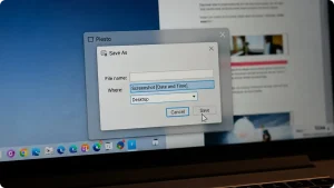 Eine Nahaufnahme eines Laptop-Bildschirms, auf dem ein „Speichern unter“-Dialogfenster (Save As) innerhalb einer Anwendung namens „Piesto“ zu sehen ist. Das Fenster zeigt Felder für den Dateinamen und den Speicherort (Desktop). Ein weißer Mauszeiger befindet sich direkt über der Schaltfläche „Save“. Im Hintergrund ist die unscharfe Windows-Taskleiste erkennbar.